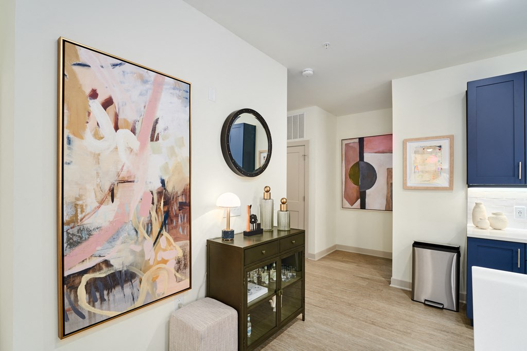 A living room with a painting on the wall and a mirror above a cabinet.