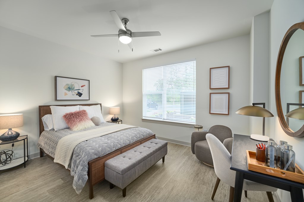 A bedroom with a bed, a chair, a table, and a ceiling fan.