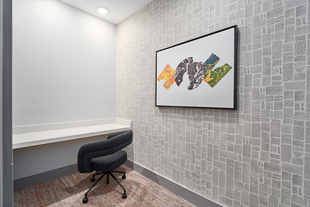A framed artwork hangs on a wall above a black office chair.