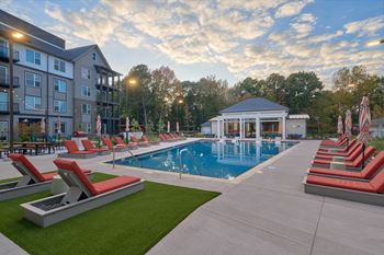 A swimming pool surrounded by red lounge chairs and a gazebo.