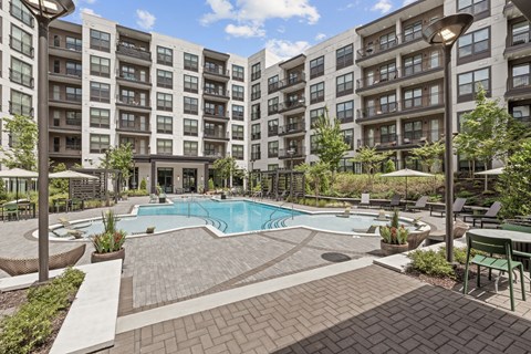 A large swimming pool surrounded by a brick patio and lounge chairs.