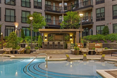 A large swimming pool in front of a building with a patio area.