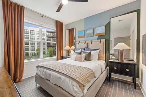 A bedroom with a large bed and a view of a building outside the window.