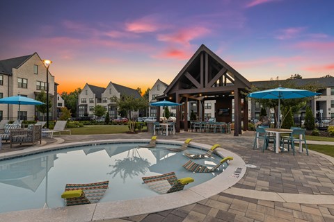 A pool with a waterfall and a water slide in the middle of a patio with chairs and umbrellas.