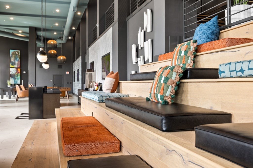 A long wooden bench with cushions and pillows is in the foreground of a modern interior space.