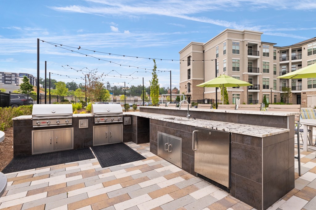 A modern outdoor kitchen area with a grill, sink, and seating area.
