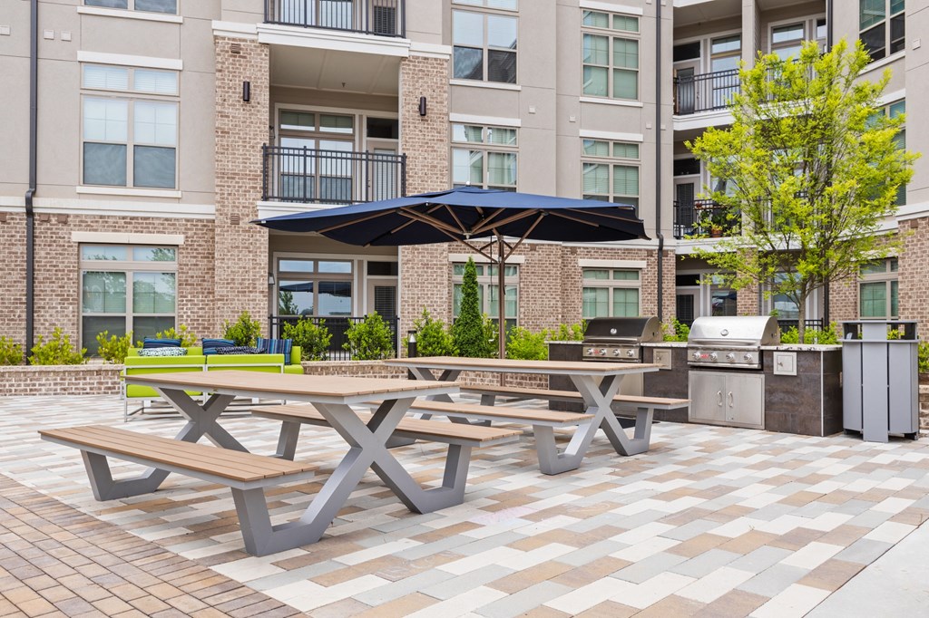 two picnic tables with umbrellas in front of an apartment building