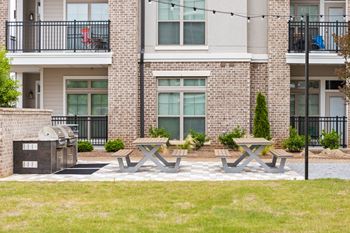 a picnic area with two picnic tables and a grill in front of an apartment building