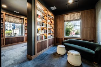 A room with a green couch, a bookshelf, and two poufs.