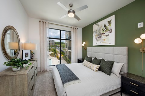 A bedroom with a large bed, a ceiling fan, and a view of the city.