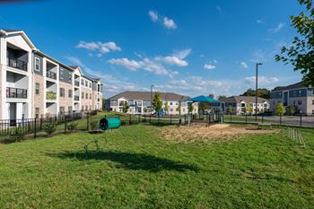 A playground with a green slide and a green barrel in the middle of a grassy area.