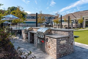 A brick BBQ grill is in the middle of a patio.