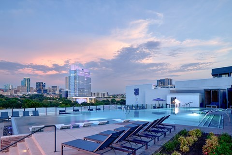 A rooftop pool area with lounge chairs and a city skyline in the background.