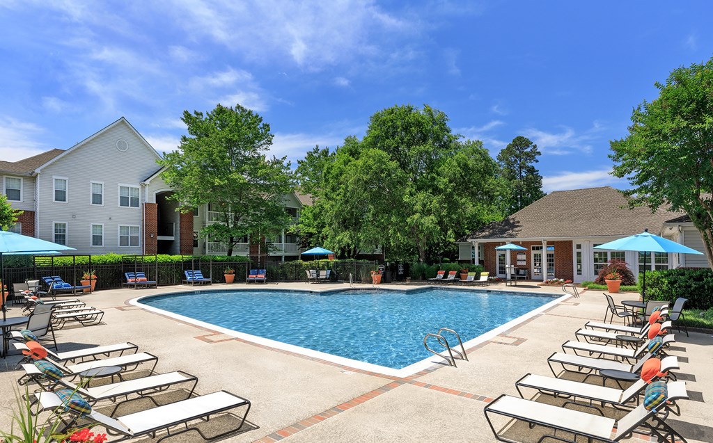 A pool surrounded by sun loungers and umbrellas with a building in the background.