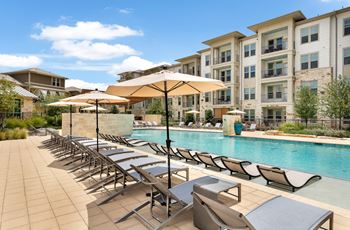 a swimming pool with chairs and umbrellas in front of an apartment building