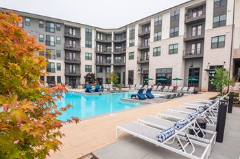 A pool area with sun loungers and apartment buildings in the background.