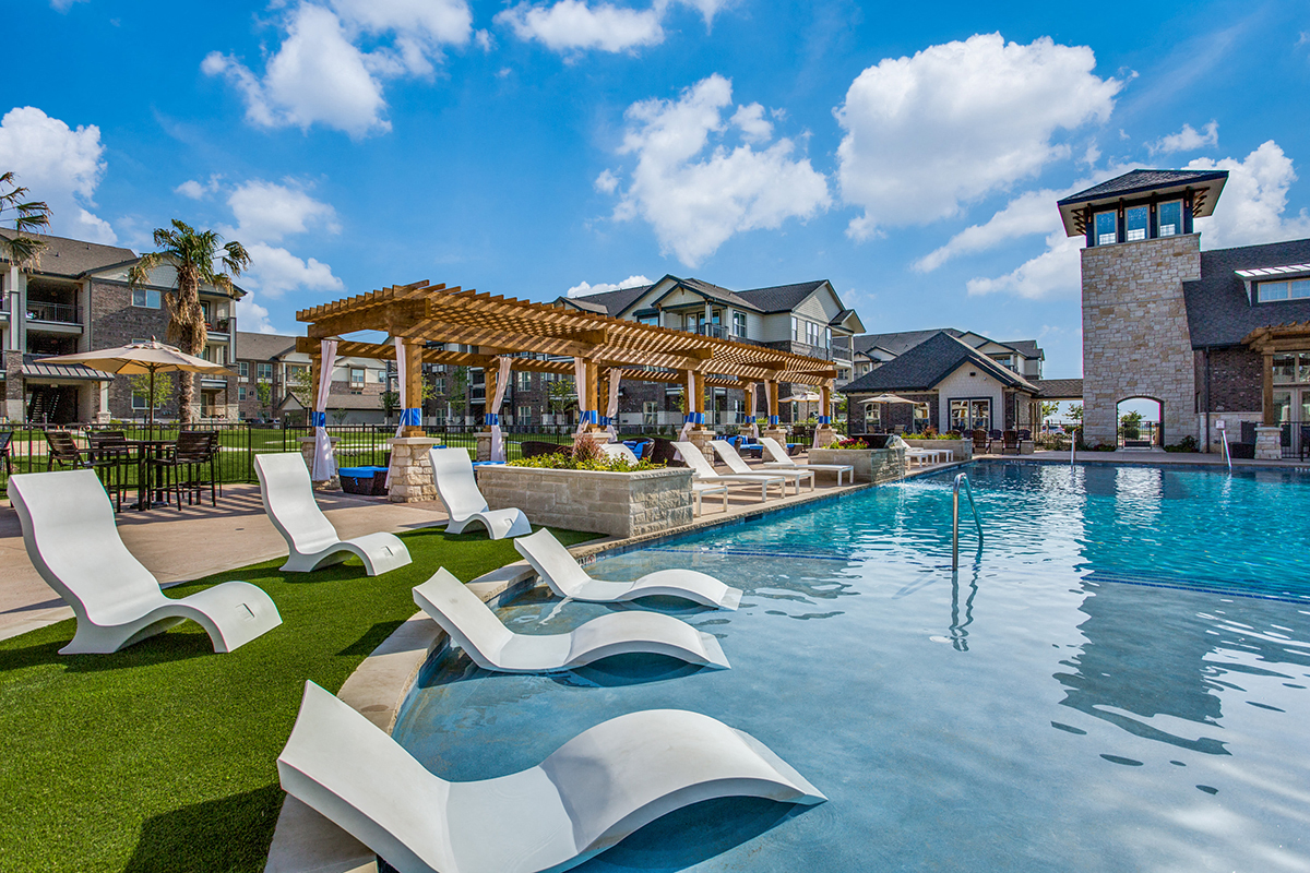 a large swimming pool with white lounge chairs and a wooden pavilion