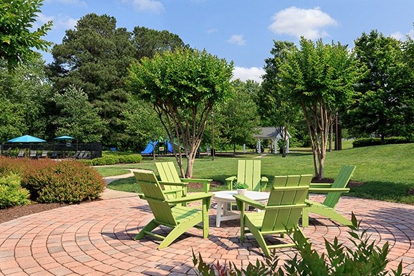a group of green adirondack chairs on a brick patio with trees in the background
