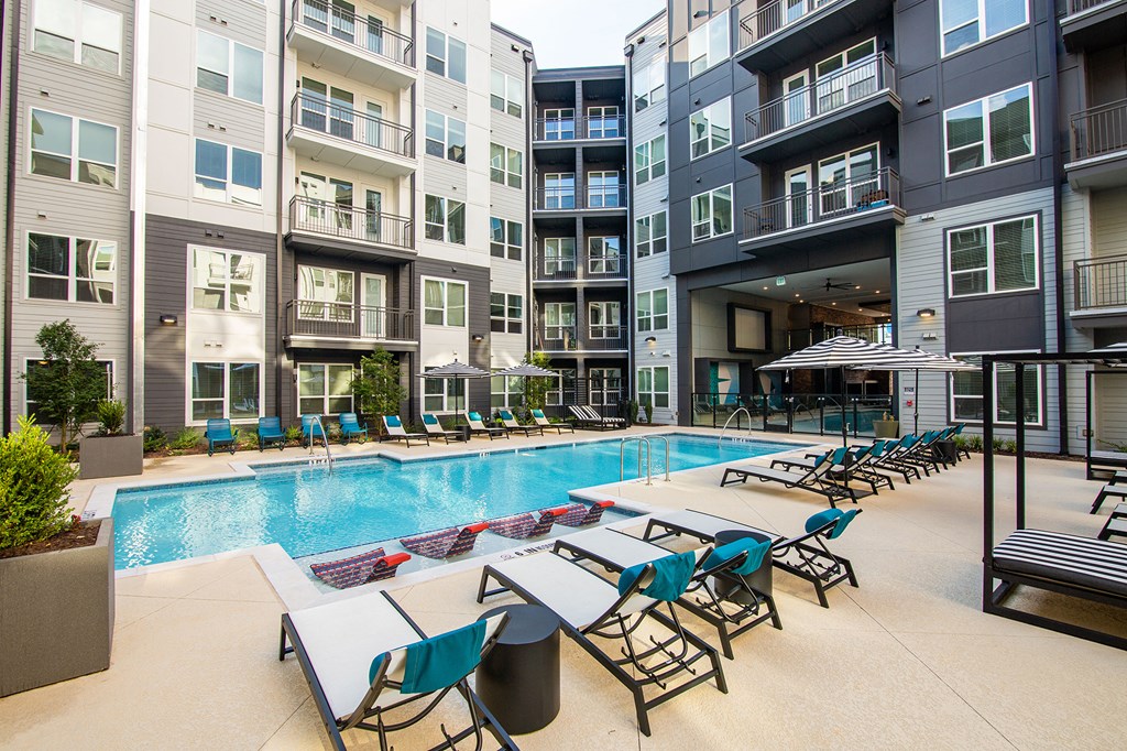 an outdoor pool with lounge chairs and tables at an apartment building