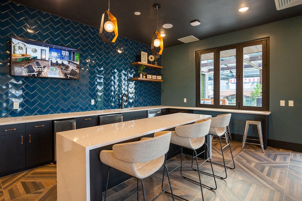 a kitchen with a long counter and chairs and a tv on the wall