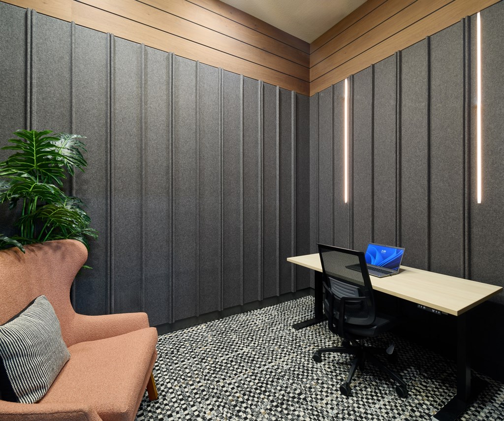 A modern office with a wooden desk, a black chair, and a pink armchair.