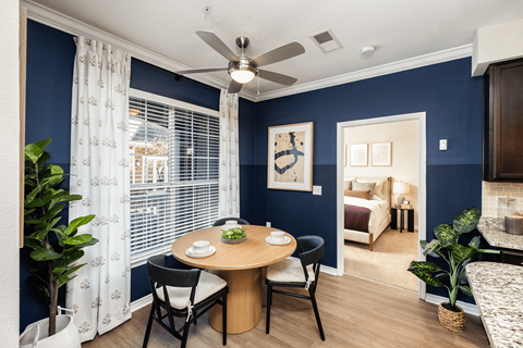 A dining room with a table set for two and a view of a bedroom through the window.