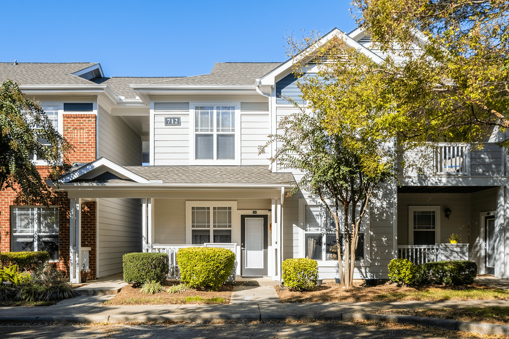 an apartment building with a porch and a tree in front of it