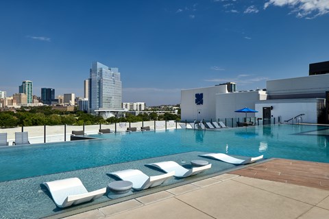 A pool with sun loungers and a city skyline in the background.