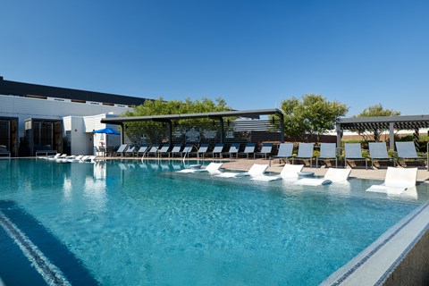 A large swimming pool with white lounge chairs and a building in the background.