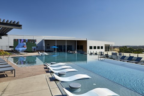 A large outdoor swimming pool with lounge chairs and a building in the background.