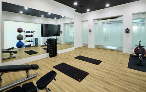 A gym with a variety of equipment including a bench, weights, and a television.