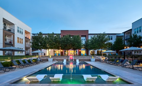 A swimming pool surrounded by lounge chairs and umbrellas in a residential area.