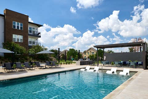 A swimming pool with lounge chairs and umbrellas in front of a building.