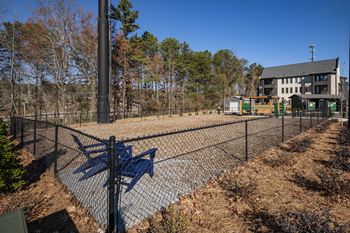 a fenced in dog park with a blue bench and a house in the background