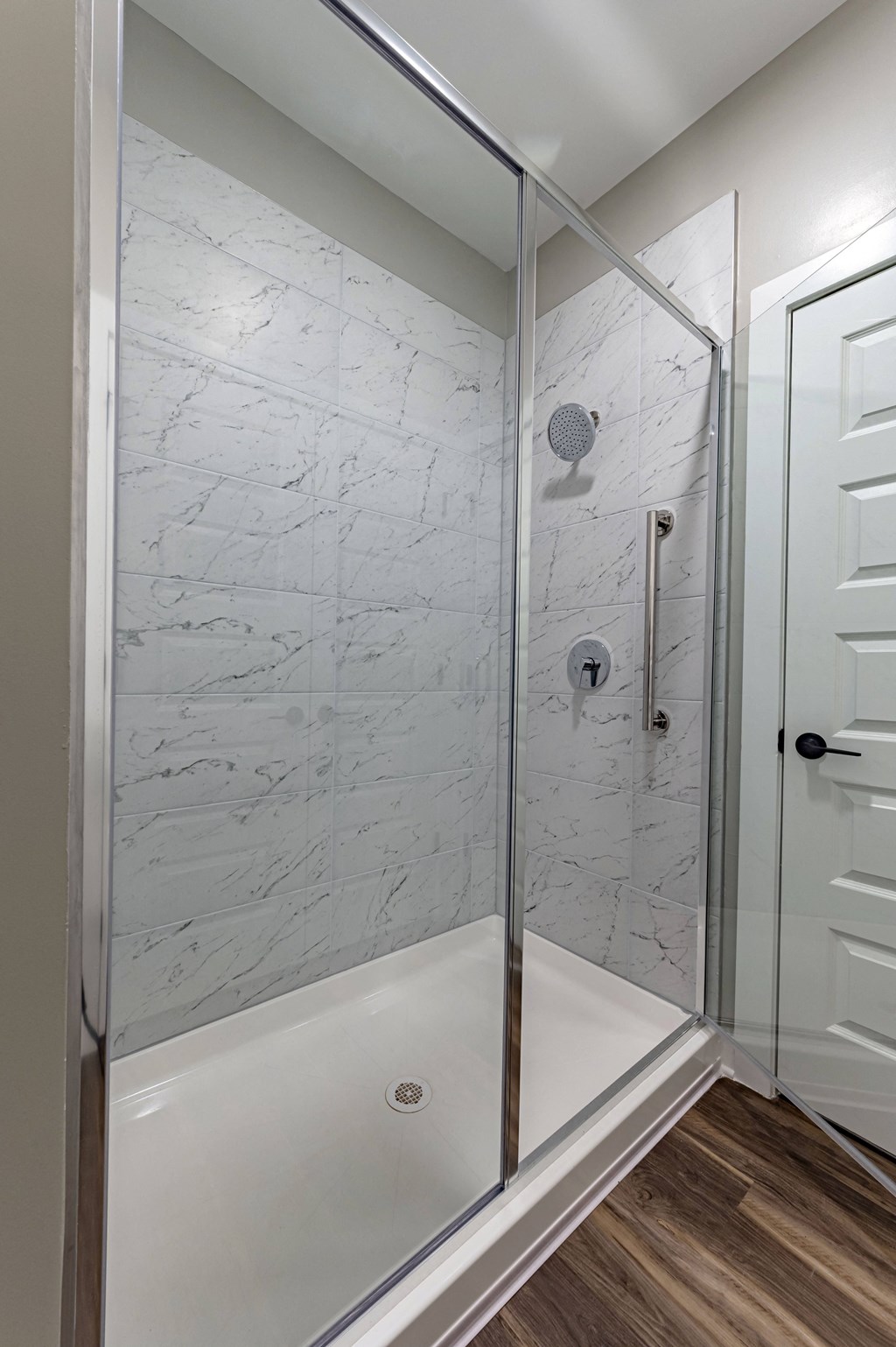 the master bathroom has a large shower with marble walls and wood flooring