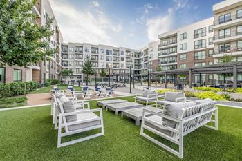an outdoor lounge area with white chairs and lawn furniture in front of an apartment building