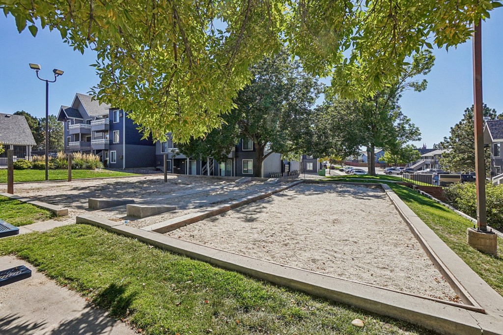A sandy area in the middle of a park with trees and houses in the background.