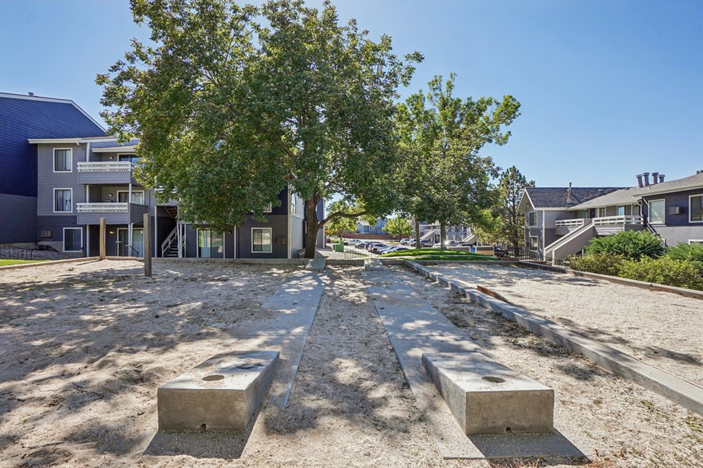 A concrete pathway leads through a sandy area with concrete blocks on either side, surrounded by trees and buildings.