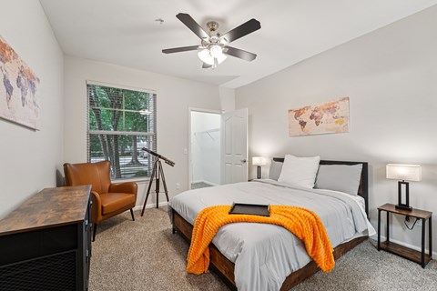 A bedroom with a bed, chair, and a ceiling fan.