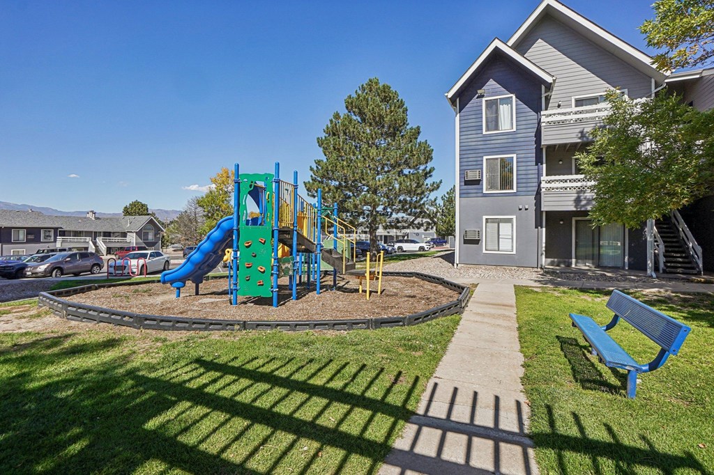 A playground with a blue slide and a green slide in the foreground with a building in the background.