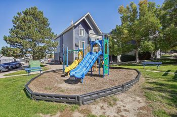 A playground with a blue and yellow slide in the foreground and a house in the background.