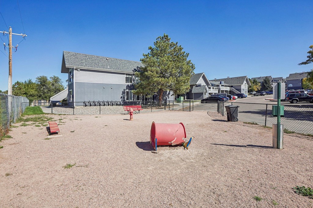 A playground with a red barrel and a grey building in the background.