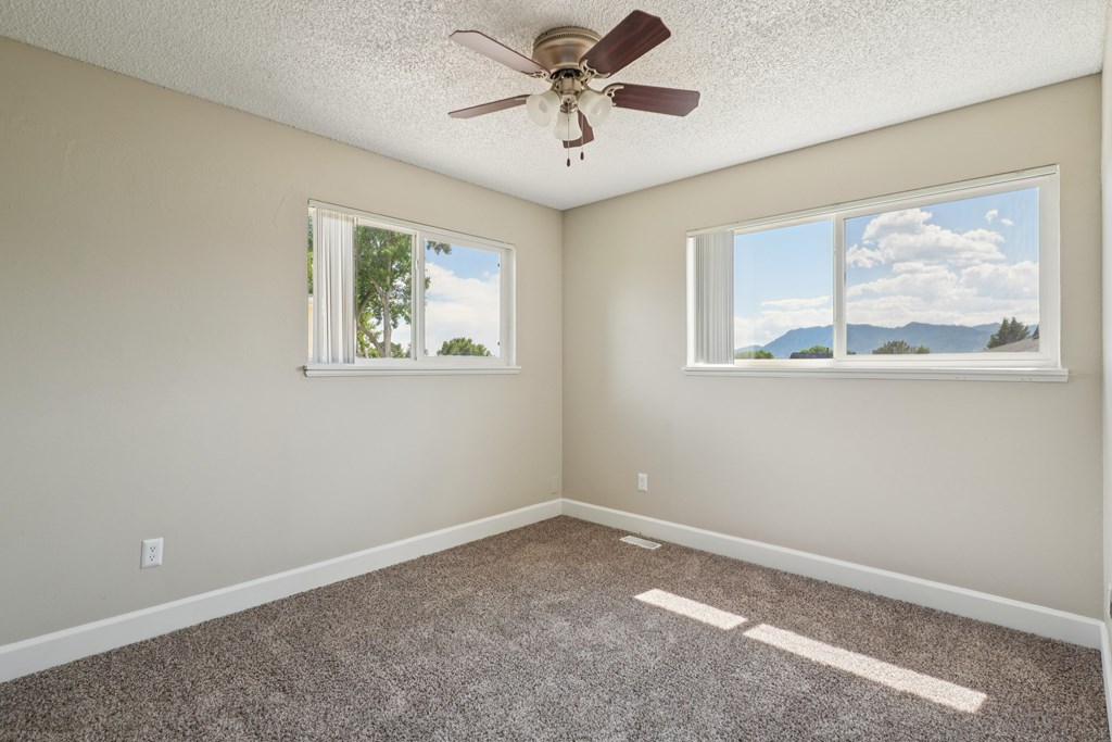 A room with a ceiling fan and two windows.at Aspen Townhomes, Colorado Springs, Colorado