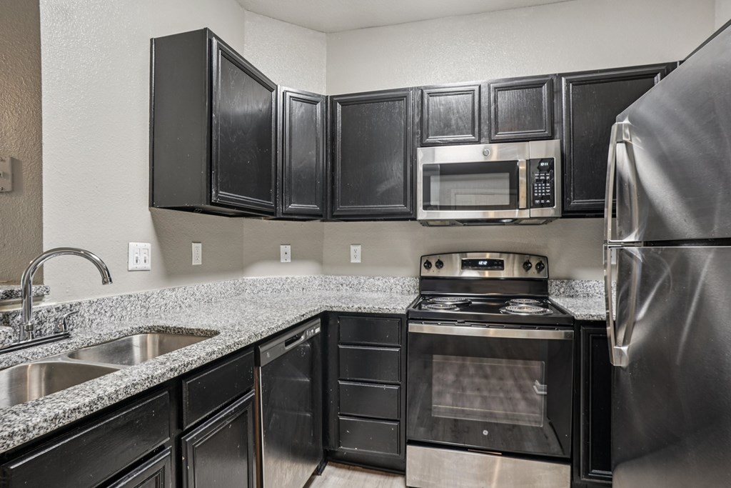 A kitchen with black cabinets and a stainless steel refrigerator.