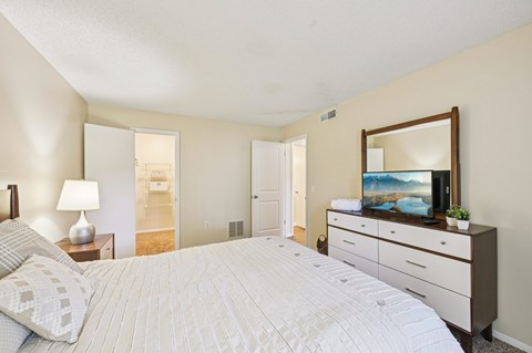 A bedroom with a large bed, a dresser with a mirror, and a lamp on a nightstand.