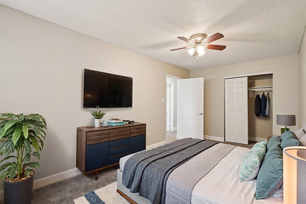 A bedroom with a bed, a dresser, a plant, and a ceiling fan.