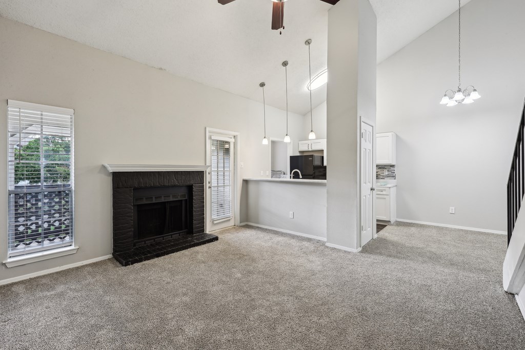 A living room with a fireplace and a kitchen area in the background at The Willows on Rosemeade, Dallas, TX 75287