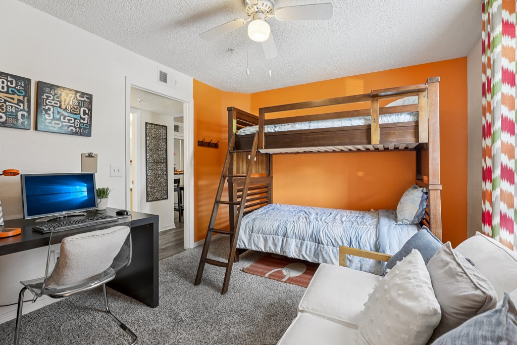 A room with a bunk bed, a desk with a computer, and a chair. at University Park Apartments, Orlando