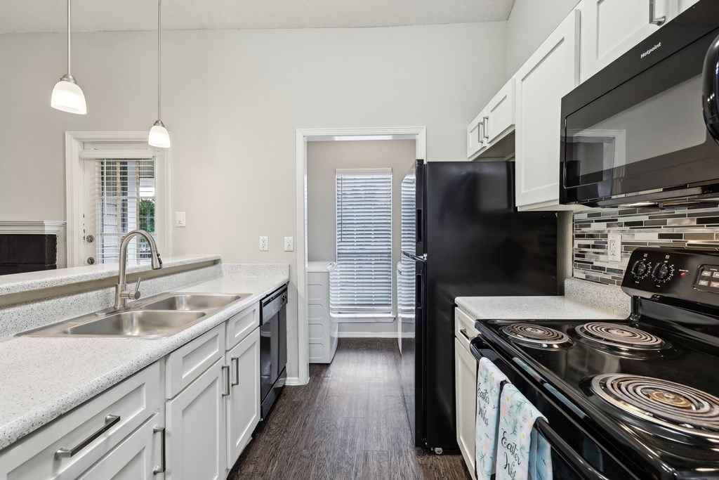 A black refrigerator sits in a kitchen with white cabinets and a black stove at The Willows on Rosemeade, Dallas, TX 75287