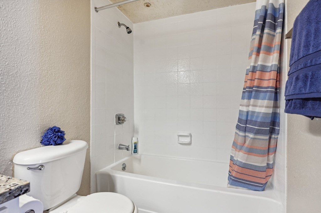a bathroom with a toilet and a tub and a shower curtain at The Glen at Highpoint, Dallas, 75243
